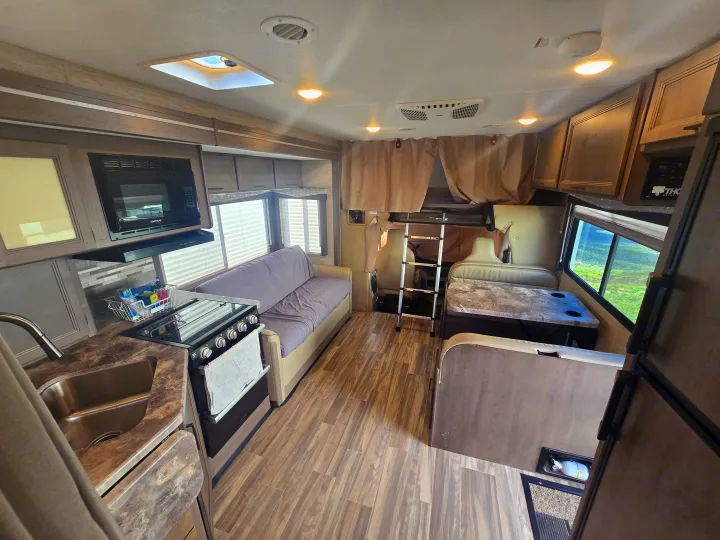 Inside an RV rental: full kitchen, sofa seating, dinette, wood flooring, and ladder accessing an overhead bunk bed.. Thor Four Winds 2023