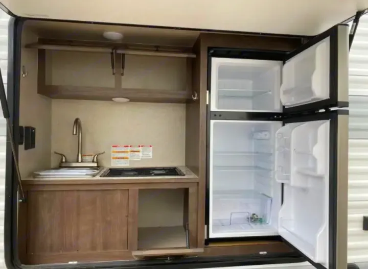 RV rental outdoor kitchen with sink, stovetop, and fridge, perfect for camping convenience and outdoor cooking.. Sunset Park RV SunRay 2022