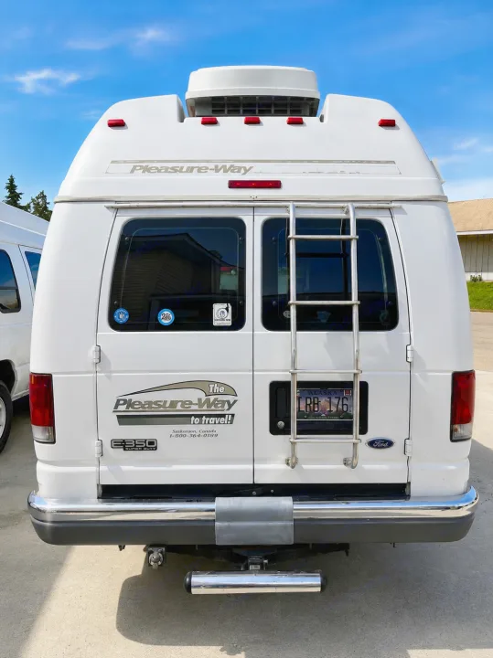 The rear of a white Pleasure-Way van RV, featuring a ladder and an Alaska license plate, ideal for rv rental or travel.. Pleasure-Way Pleasure-Way Class B 2002