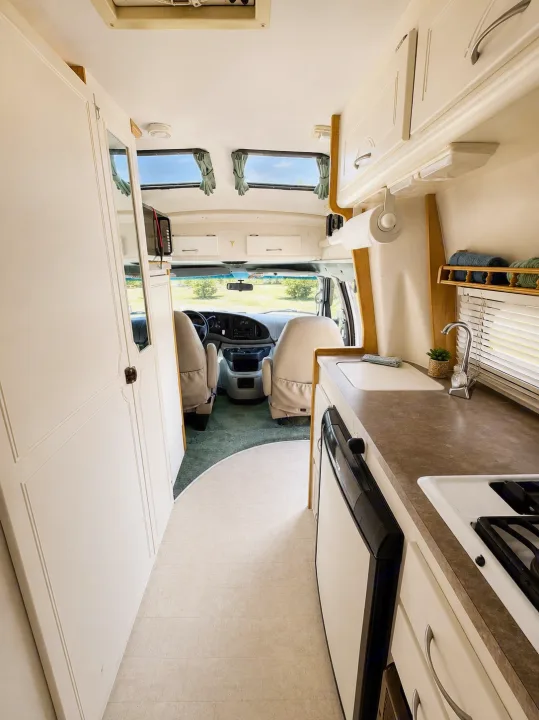 Explore this bright RV rental interior featuring a compact kitchen, driver's cabin, and ample storage for your road trip adventures.. Pleasure-Way Pleasure-Way Class B 2002
