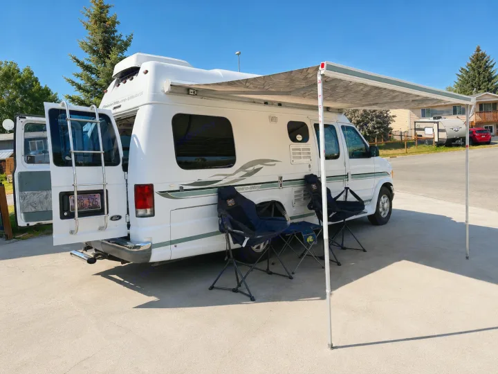 Relax under the awning of your white camper van RV rental. Perfect for a cozy road trip, with chairs ready for outdoor leisure.. Pleasure-Way Pleasure-Way Class B 2002