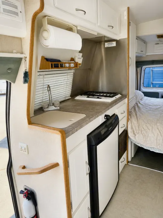 Compact RV rental kitchen with sink, stove, fridge, and bed in view. Practical setup for adventurers.. Pleasure-Way Pleasure-Way Class B 2002