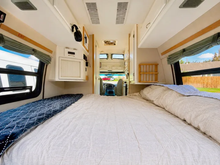 Spacious RV rental bedroom featuring a large, inviting bed, overhead storage, and bright windows with outdoor views.. Pleasure-Way Pleasure-Way Class B 2002