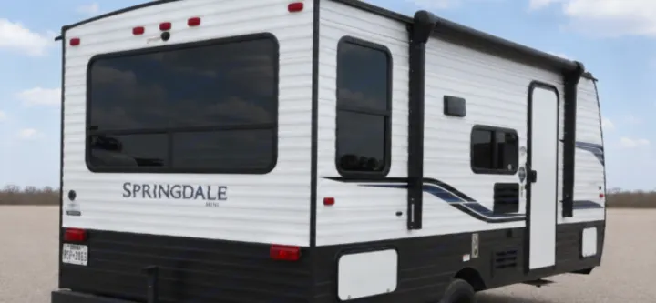 White and black Springdale travel trailer rv rental parked outdoors, showcasing its exterior, windows, and side door.. Keystone RV Springdale 2020
