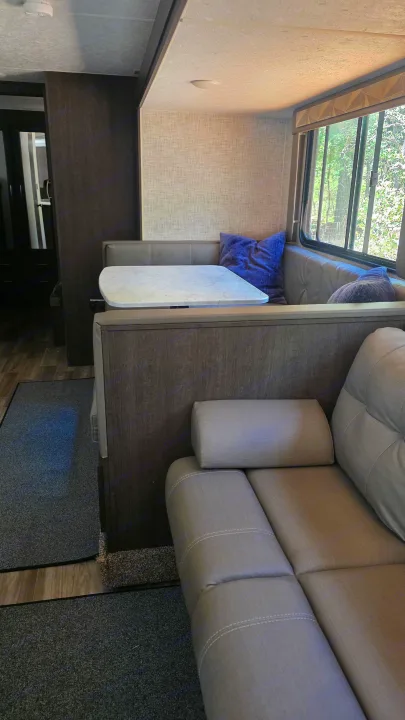 RV rental interior: A cozy dinette with a white table and gray benches next to a comfy sofa, perfect for travel.. Forest River Wildwood X-Lite 2019