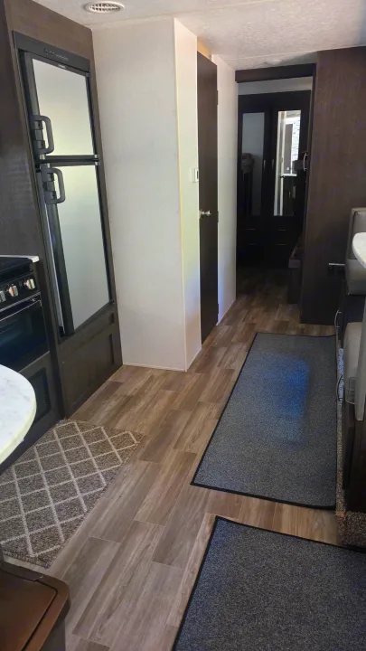 Inside this RV rental, a compact kitchen with a two-door fridge is on the left, leading to a dining area and hallway on wood-look floors.. Forest River Wildwood X-Lite 2019