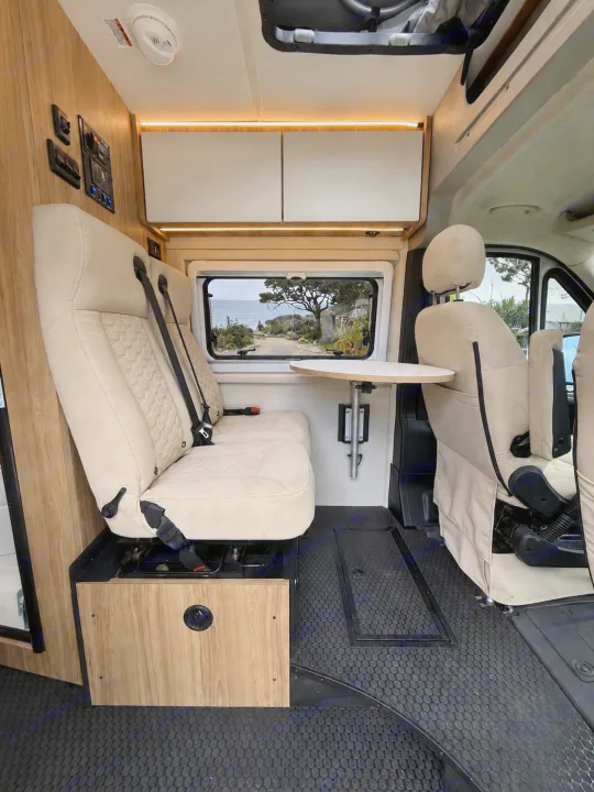 Cozy RV rental interior with dinette seating and a window showcasing a beautiful coastal view, perfect for adventure.. Coachmen Pixel 2025