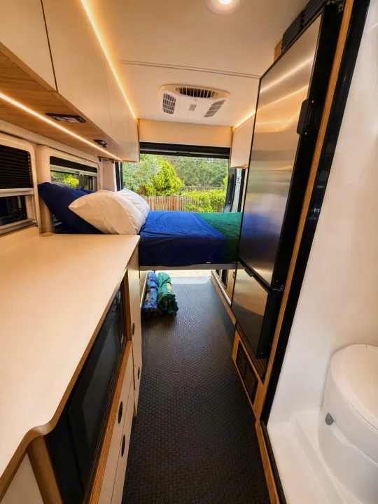 RV rental: Modern camper van interior with a cozy bed, sleek kitchen counter, large fridge, and compact bathroom with a toilet.. Coachmen Pixel 2025