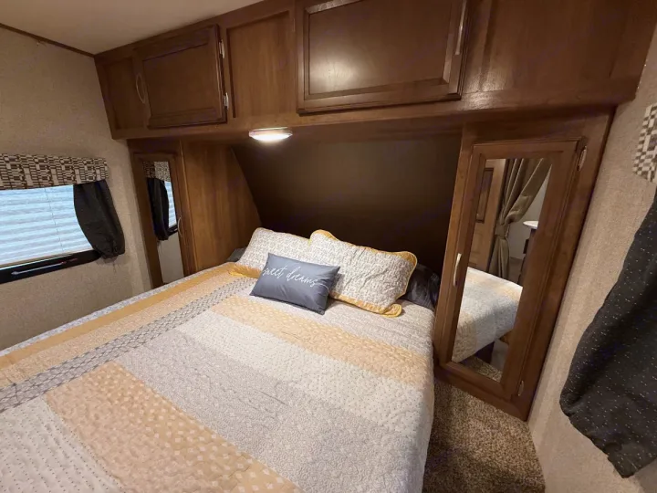 Cozy RV rental bedroom with patterned bedding, overhead cabinets, a window, and mirrored closets, creating a warm, inviting space.. Coachmen Apex Ultra Lite 2016