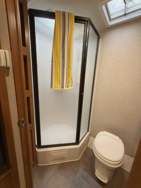 Experience the convenience of an RV rental bathroom: compact shower with frosted door, toilet, and overhead vent.. Coachmen Apex Ultra Lite 2016