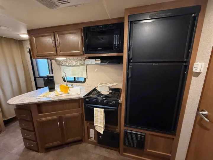 A cozy RV rental kitchen with a black refrigerator, microwave, stove, sink, and wood cabinets for your travels.. Coachmen Apex Ultra Lite 2016