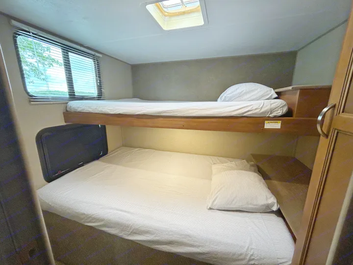 Cozy RV rental bunk beds feature striped bedding, a window with outdoor views, and a ceiling skylight.. Keystone RV Summerland 2018