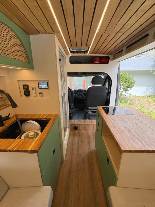 RV rental: Stylish camper van interior with wood ceiling, modern kitchen (sink, cooktop), and driver's cabin visible.. Ram Promaster 2500 2017