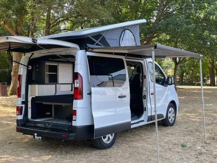 White campervan RV rental with a raised pop-top roof, extended side awning, and open doors revealing its custom interior conversion.. HANROAD TREK 5 2026
