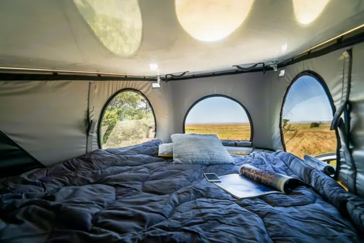 Cozy RV rental pop-top tent interior: comfy bed, phone, magazine, and scenic views from round windows.. HANROAD TREK 5 2026