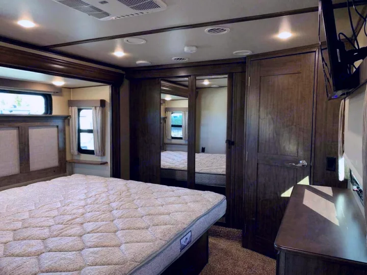 Spacious RV rental bedroom featuring a comfortable bed, mirrored wardrobe, and windows for your trips.. Grand Design Solitude 2018