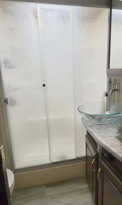 RV rental bathroom with frosted shower, vessel sink, dark vanity, and gray floor. Yellow streaks visible on shower panels.. Grand Design Solitude 2018