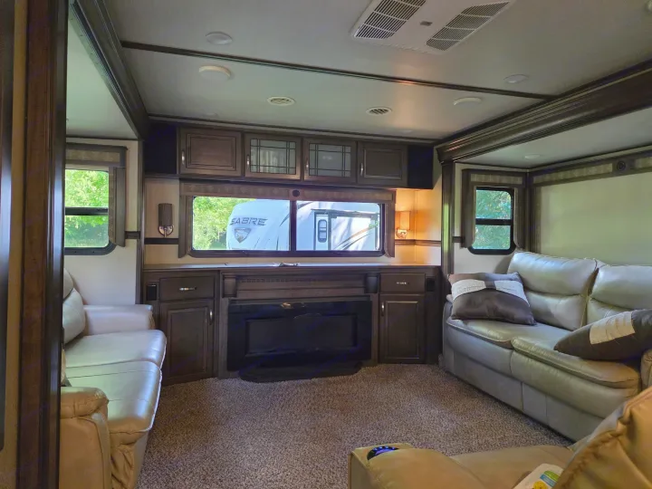 Spacious RV rental living room featuring comfy leather sofas, a cozy fireplace, and large windows. Ideal for travel!. Grand Design Solitude 2018