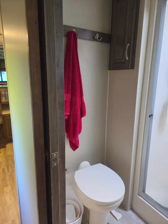 Small bathroom in an RV rental, featuring a toilet, red towel, and shower stall. Ideal for travel or camping.. Grand Design Solitude 2018
