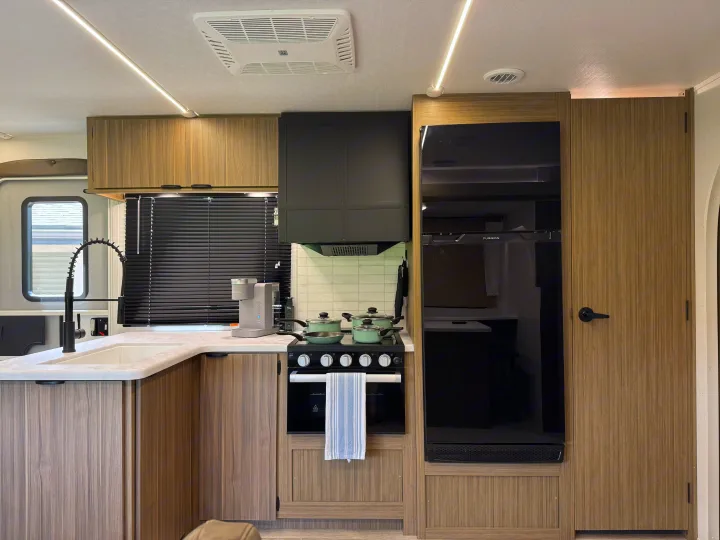 Modern rv rental kitchen with sleek black appliances, wood-look cabinets, sink, stove, and a large refrigerator.. Forest River Wildwood FSX Platinum 2026