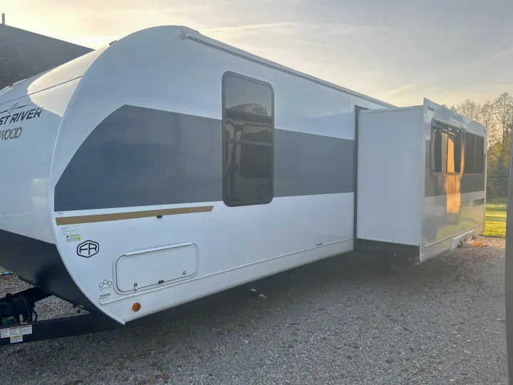 Bright white & grey rv rental travel trailer, with its slide-out extended, parked on a gravel lot under sunlight.. Forest River Wildwood FSX Platinum 2026