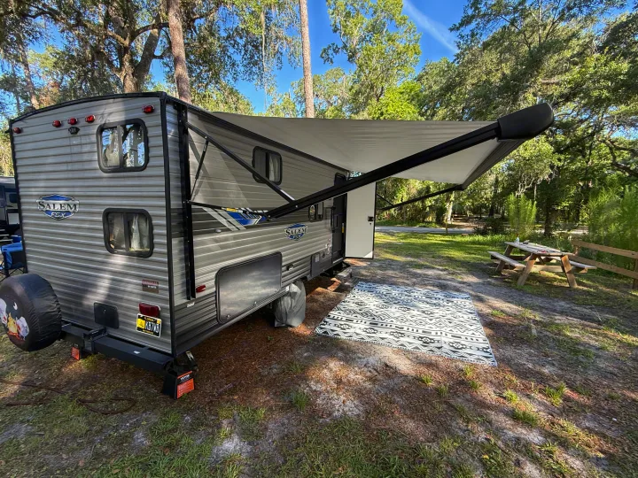 RV rental travel trailer parked at a sunny Florida campsite with an extended awning, outdoor rug, and picnic table.. Forest River Salem FSX 2022
