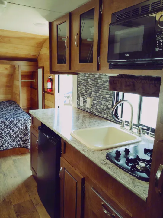 Inside an RV rental, this cozy space features a compact kitchen with microwave, sink, stovetop, and fridge, plus a sleeping area.. Forest River Salem FSX 2017