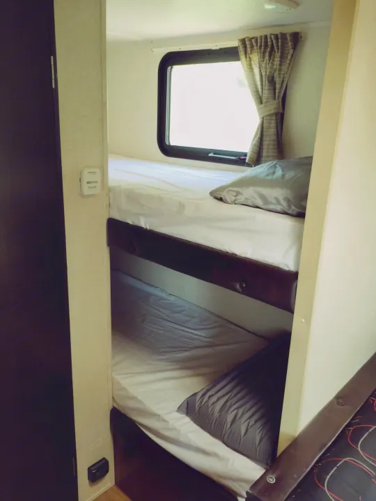 Compact RV rental sleeping area with two bunk beds, complete with fresh bedding, a window, and a thermostat.. Forest River Salem FSX 2017