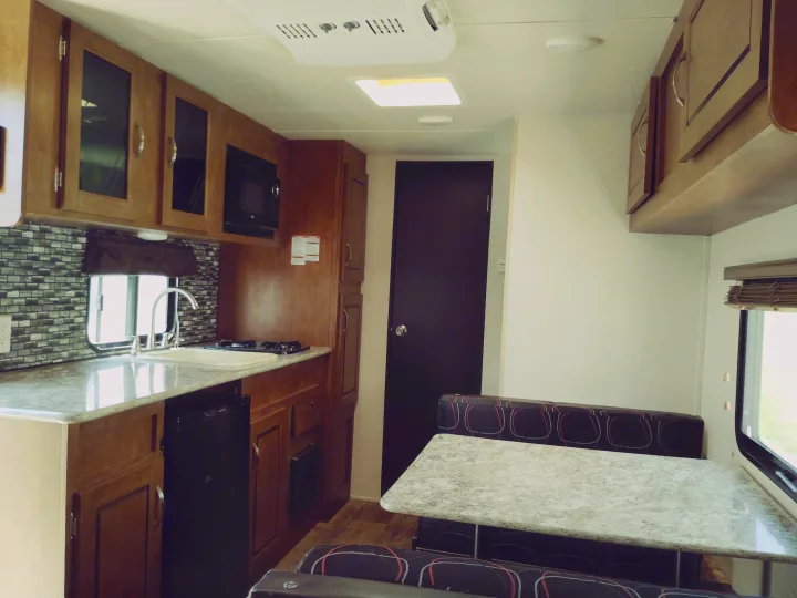 RV rental interior: a modern kitchen with sink, stovetop, microwave, fridge, wood cabinets, and a cozy dining booth.. Forest River Salem FSX 2017