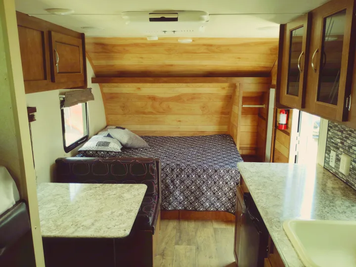 Cozy RV rental interior featuring a bed with patterned bedding, a dinette, and a kitchen counter with a sink. Ideal travel trailer.. Forest River Salem FSX 2017