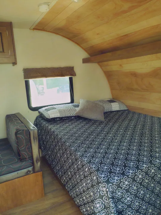 This RV rental's interior shows a cozy bed with patterned linens, a window, and wood-paneled ceiling/wall.. Forest River Salem FSX 2017