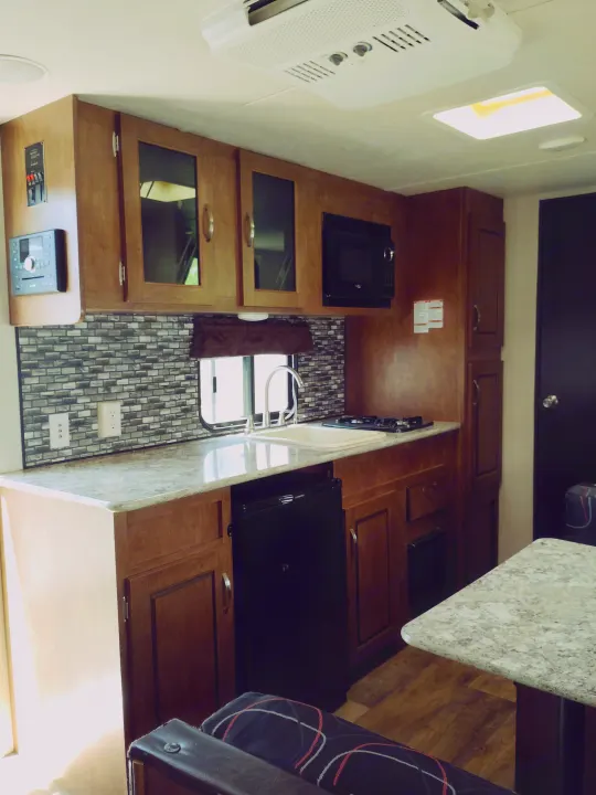 This RV rental kitchen features wood cabinets, a mosaic tile backsplash, sink, stovetop, microwave, and mini-fridge.. Forest River Salem FSX 2017