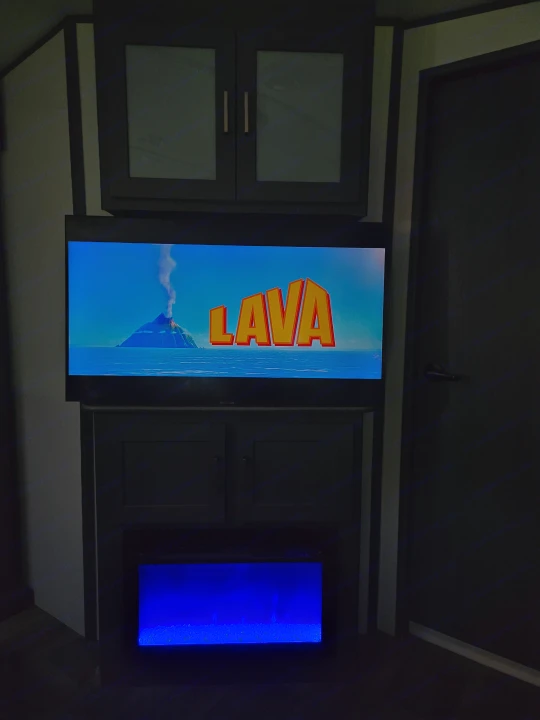RV rental entertainment center with TV showing "Lava," storage cabinets, and an electric fireplace glowing blue.. Keystone RV Bullet Ultra Lite 2023