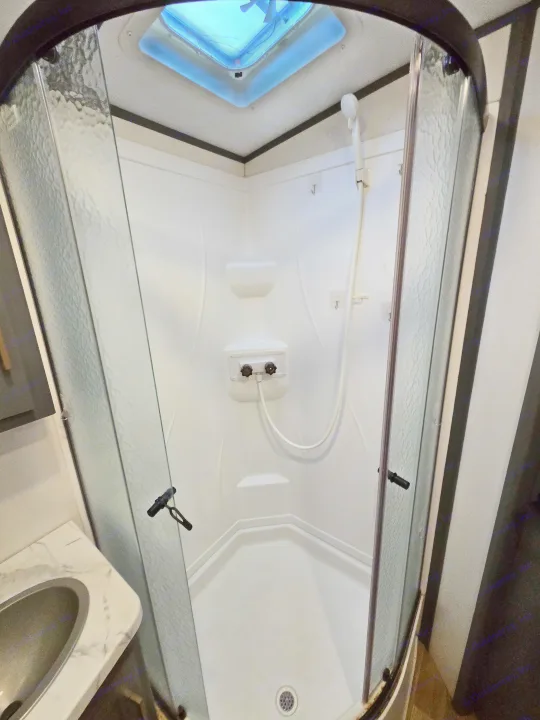 Compact RV rental shower stall: white interior, textured glass doors, showerhead, and overhead vent.. Keystone RV Bullet Ultra Lite 2023