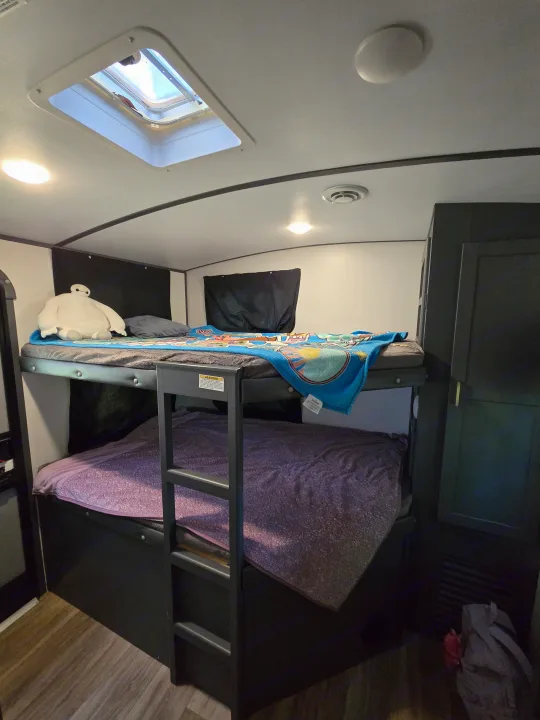 Cozy RV rental interior with bunk beds, a Baymax plush on the top, warm blankets, and a bright skylight.. Keystone RV Bullet Ultra Lite 2023