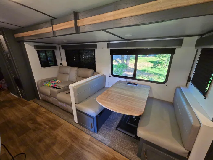 This RV rental interior showcases a modern living/dining area with a grey recliner sofa, wood dinette table, and laminate floor.. Keystone RV Bullet Ultra Lite 2023