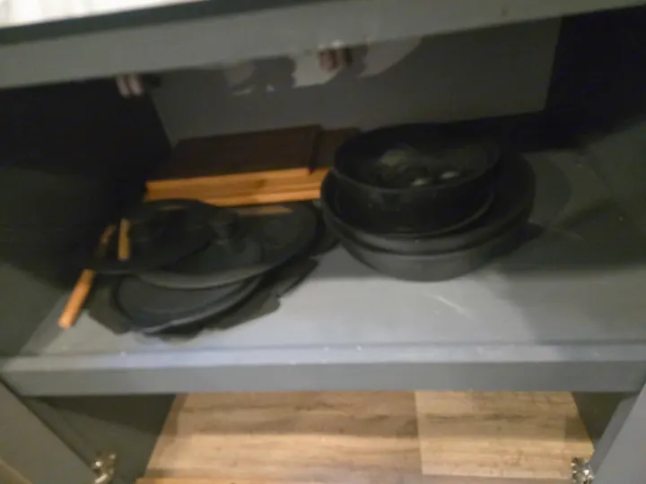 Sturdy cast iron pots, pans, & lids neatly stored with wooden cutting boards in an RV rental kitchen cabinet.. Keystone RV Bullet Ultra Lite 2023
