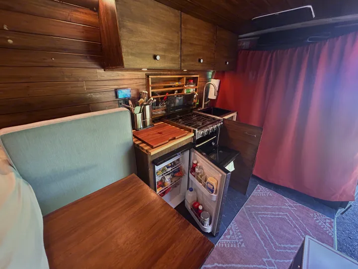 Compact RV rental interior with a fully equipped kitchen, dining area, open fridge, and warm wood finishes.. RAM Promaster 2022