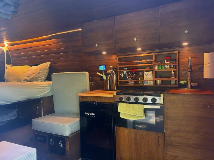 Cozy RV rental interior featuring a functional kitchen, comfortable bed, and warm wooden finishes.. RAM Promaster 2022