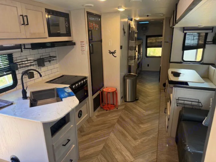 Inside a modern rv rental, featuring a bright kitchen with white subway tile, a dining area, and a hallway leading to bunk beds.. Heartland RVs Mallard 2023