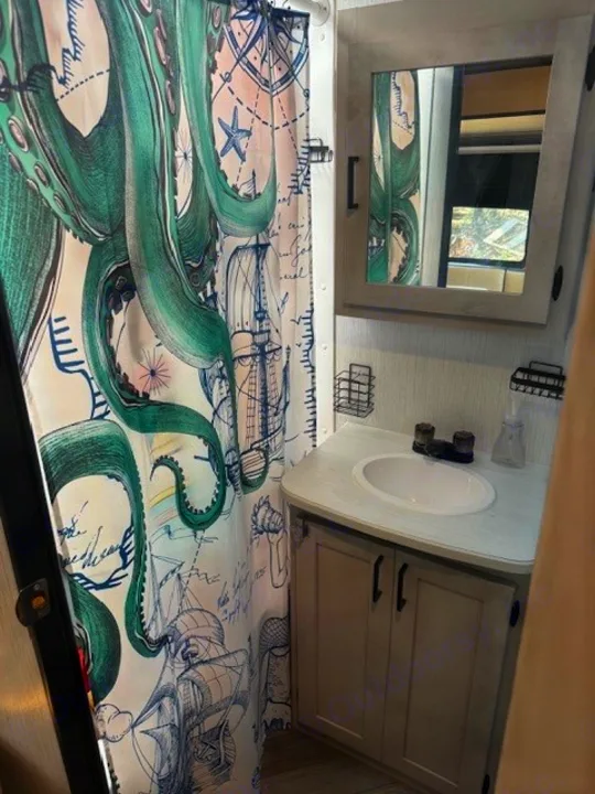 Compact rv rental bathroom features a unique green octopus and nautical shower curtain, vanity with sink, and mirror.. Heartland RVs Mallard 2023