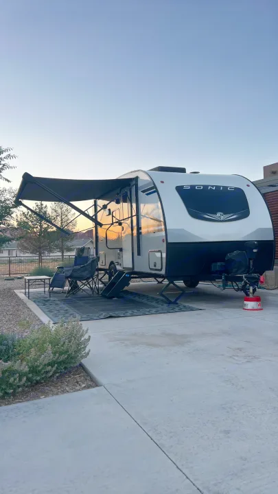 RV rental ready for relaxation: A Sonic travel trailer with awning, chairs, and rug reflects the warm sunset glow.. Sonic Lite 2021