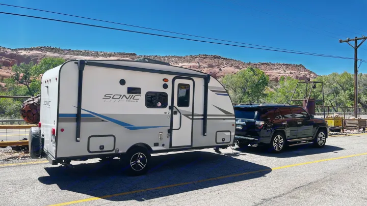 RV rental adventure: A Sonic Lite travel trailer is hitched to a black SUV, ready for a desert road trip in a scenic landscape.. Sonic Lite 2021