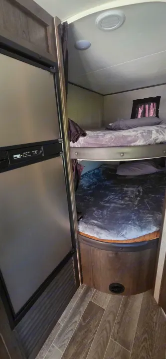RV rental interior: A silver refrigerator stands next to bunk beds, featuring purple and grey blankets, and wood-look flooring.. Jayco Jay Flight SLX 2021