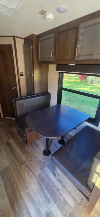 Cozy RV rental interior with a dinette, dark cabinets, wood flooring, and a window view of greenery.. Jayco Jay Flight SLX 2021