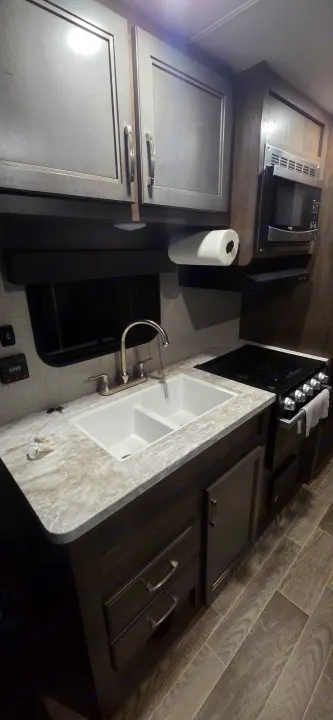 RV rental kitchen: a compact, clean space featuring a double sink, stove, microwave, and modern dark wood cabinets.. Jayco Jay Flight SLX 2021