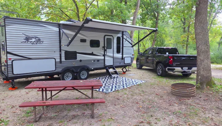 RV rental: Travel trailer with extended awning, pickup truck, picnic table, and fire pit at a wooded campsite.. Jayco Jay Flight SLX 2021