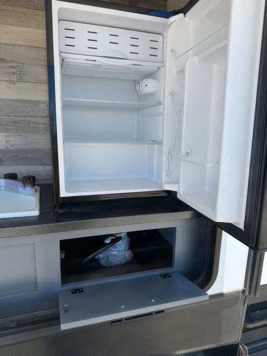 RV rental outdoor kitchen with open mini-fridge, sink, and under-counter storage.. Crossroads RV Volante 2023