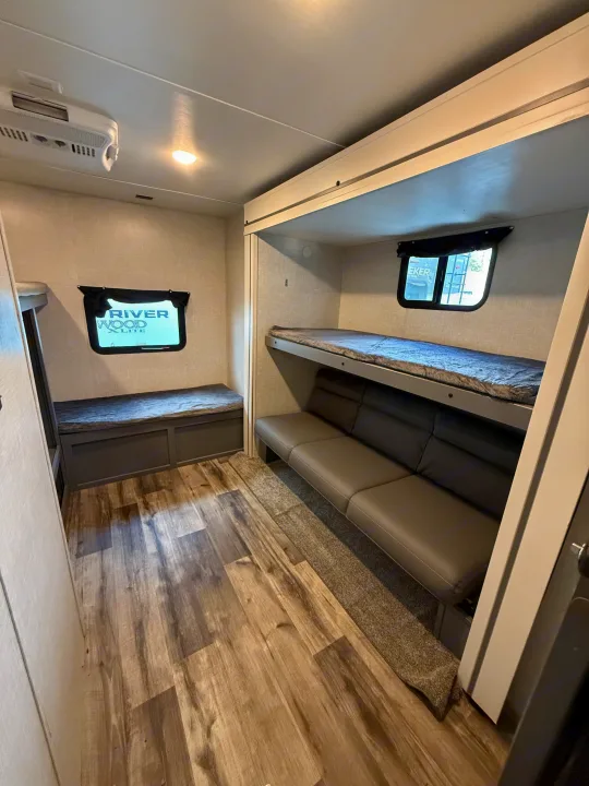 RV rental interior showcasing bunk beds over a sofa, a side bench, and wood-look flooring for comfortable travel.. Crossroads RV Volante 2023