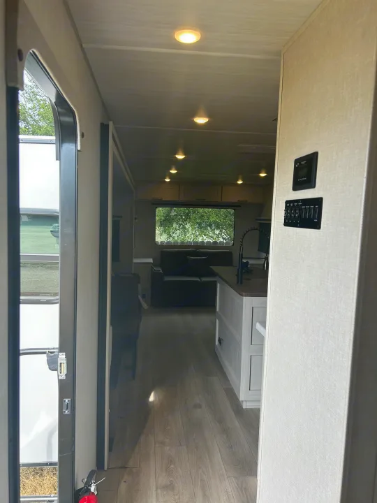 Step into this bright RV rental! Modern interior with open kitchen & living area, showing controls near the entry door.. Forest River Grand Surveyor 2025